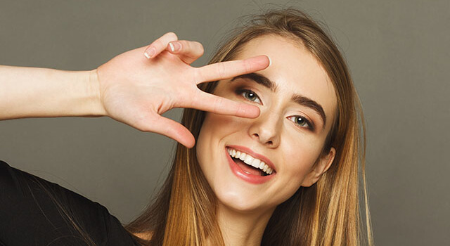 Pretty Cheerful Woman Gesturing With Two Fingers Near Eyes. Youn